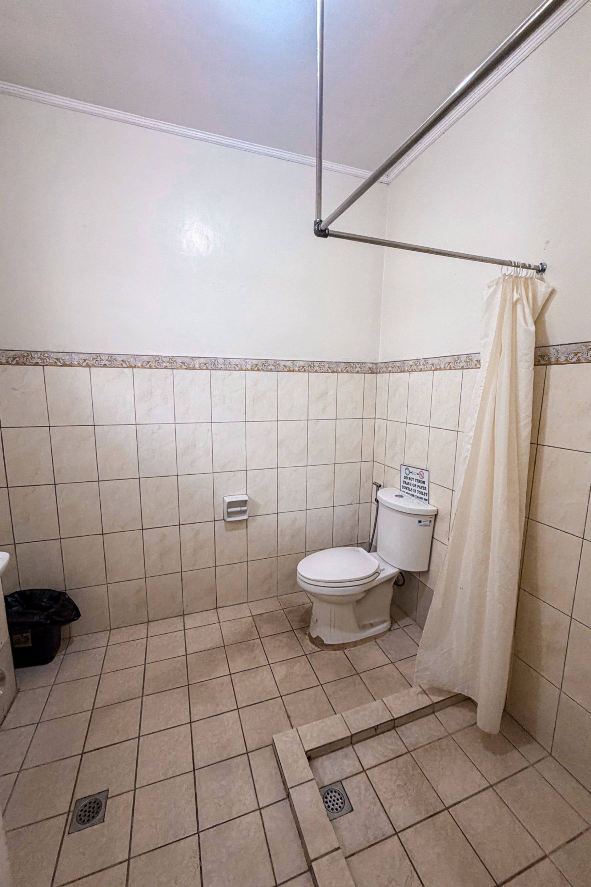 Kylpyhuone, jossa on wc, suihkuverho ja laatoitettu lattia.