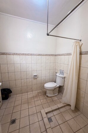 Un baño con inodoro, cortina de ducha y piso de baldosas.