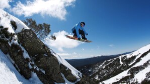 A snowboarder mid-air performing a jump on a snowy mountain slope.