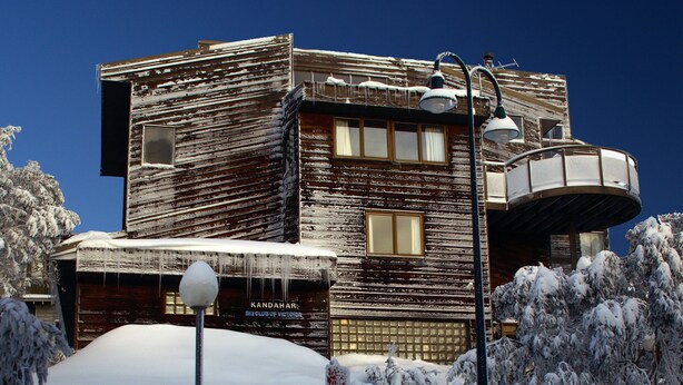 A wooden building with a ski club sign, surrounded by snow-covered trees.