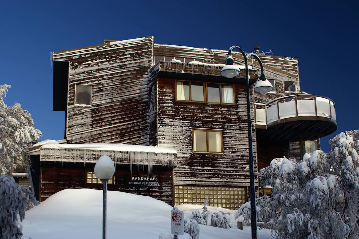 Een houten gebouw met een bord van een ski club, omgeven door met sneeuw bedekte bomen.