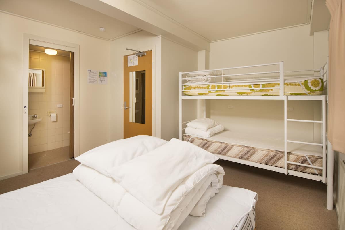 Een hotelkamer met een stapelbed, een enkel bed, een badkamer met een wastafel, en een deur die leidt naar een andere kamer.