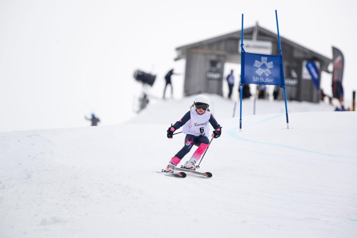 A skier in motion on a snowy slope with a blue flag and a building in the background.