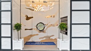 Ein Hotel Eingang mit modernem Design, inklusive Glastür, einer Kristallleuchter und zwei Topfpflanzen.