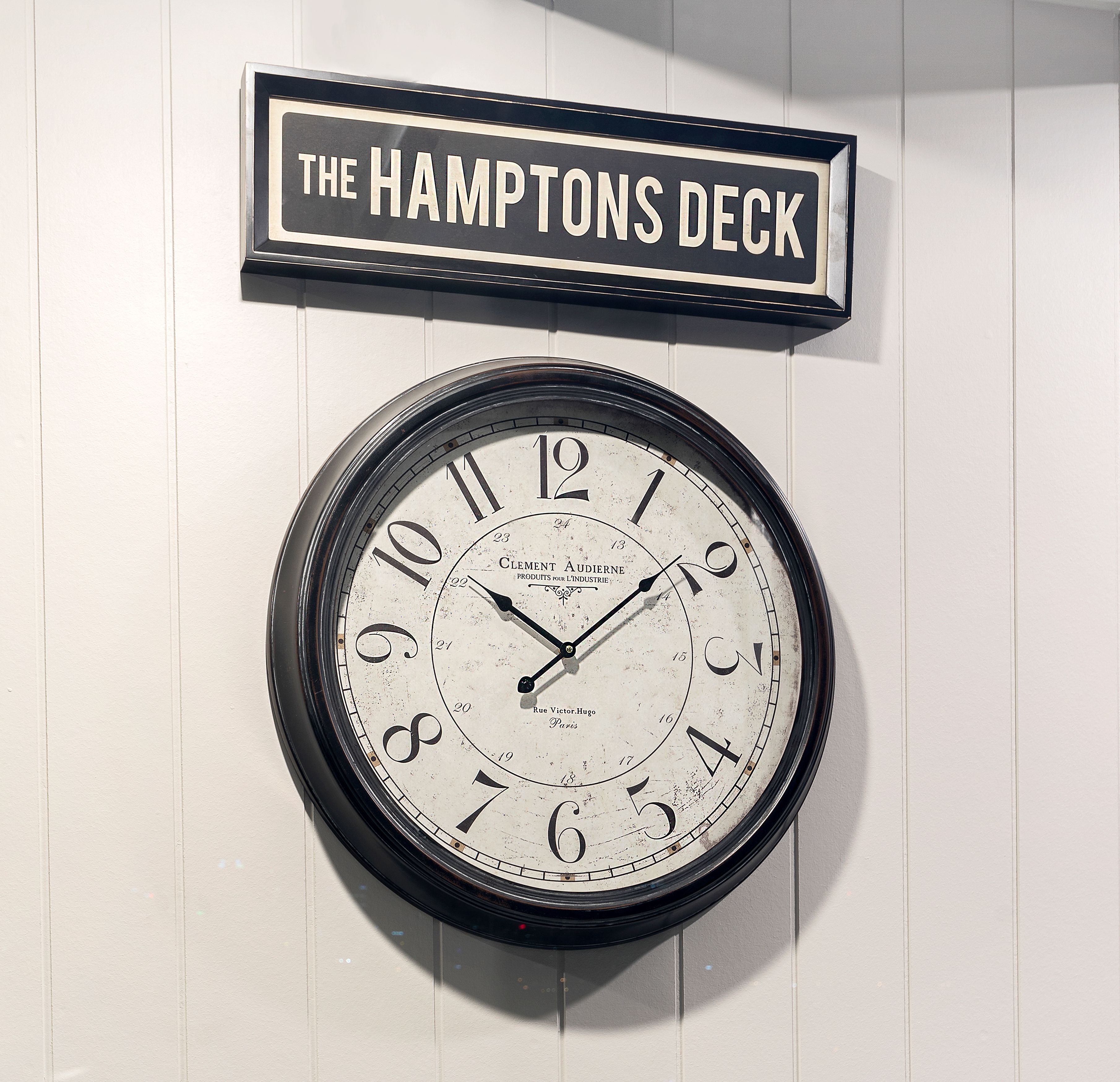 A wall-mounted clock with a sign above it reading "THE HAMPTONS DECK".