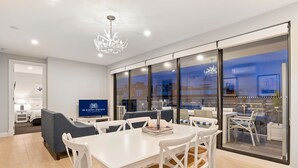 Ein modernes Hotelzimmer mit Essbereich, einer Couch, einem Fernseher und einem großen Fenster mit Blick auf die Stadt.