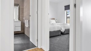 A modern bedroom with two beds, a ceiling fan, and a view of the outside. - Coastal Vibe Apartments (Warrnambool)