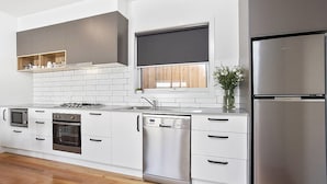 A modern kitchen with white cabinetry, stainless steel appliances, and a wooden floor. - Coastal Vibe Apartments (Warrnambool)