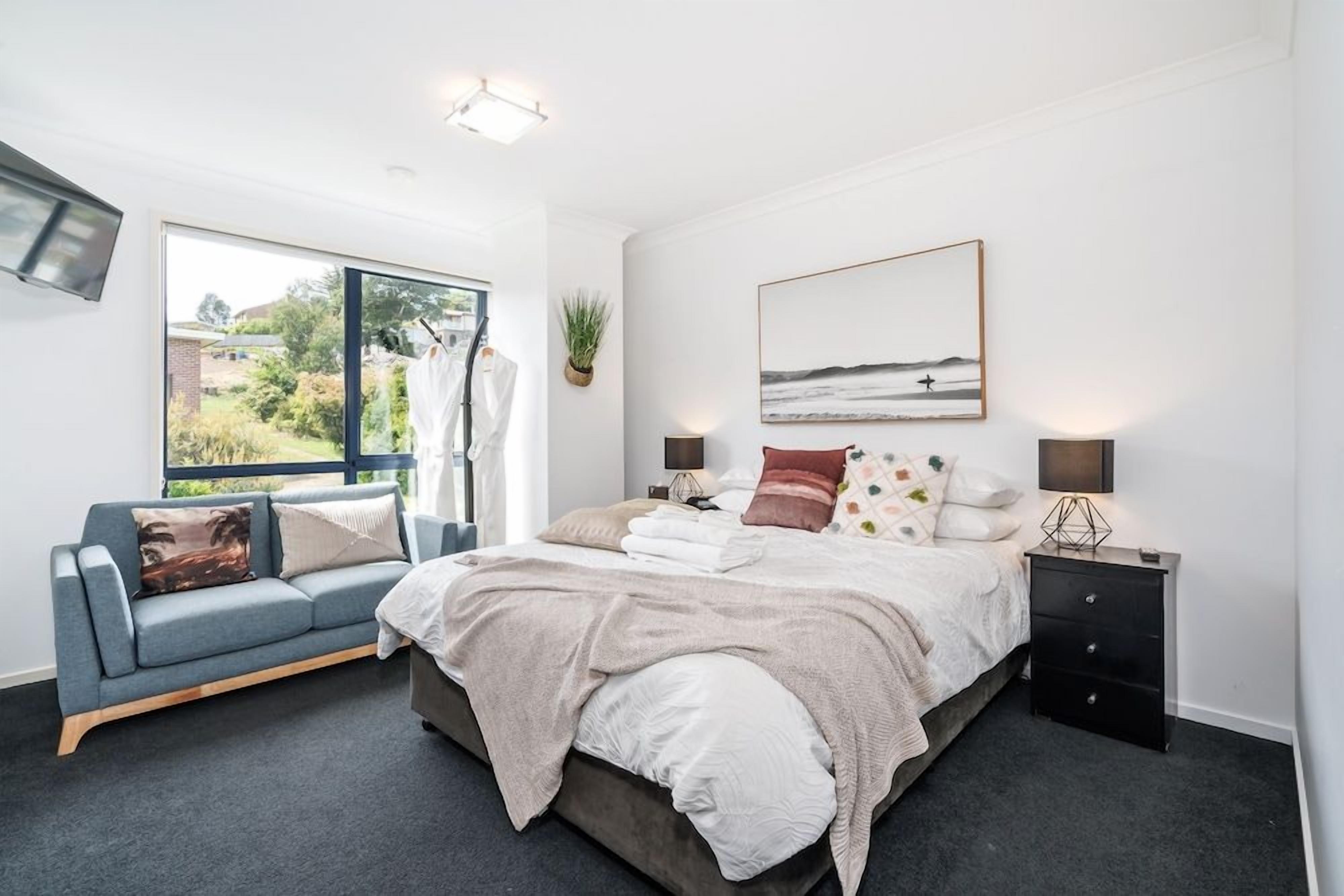 A bedroom with a bed, bedside tables, a sofa, a window, and a wall-mounted TV.