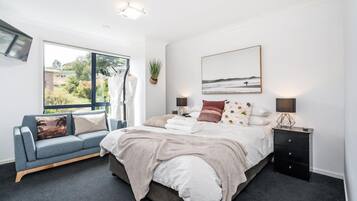 A bedroom with a bed, bedside tables, a sofa, a window, and a wall-mounted TV.