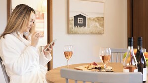 A person in a white robe at a round table with a wine glass, a bottle of wine, and a plate with food. - Madsen Retreat (Penguin)