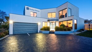A modern two-story building with a garage, large windows, and a well-lit entrance. - Madsen Retreat (Penguin)