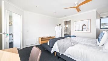 Ett modernt hotellrum med en säng, ett skrivbord, en stol, ett träbord vid sängen, en takfläkt och ett fönster med utsikt.