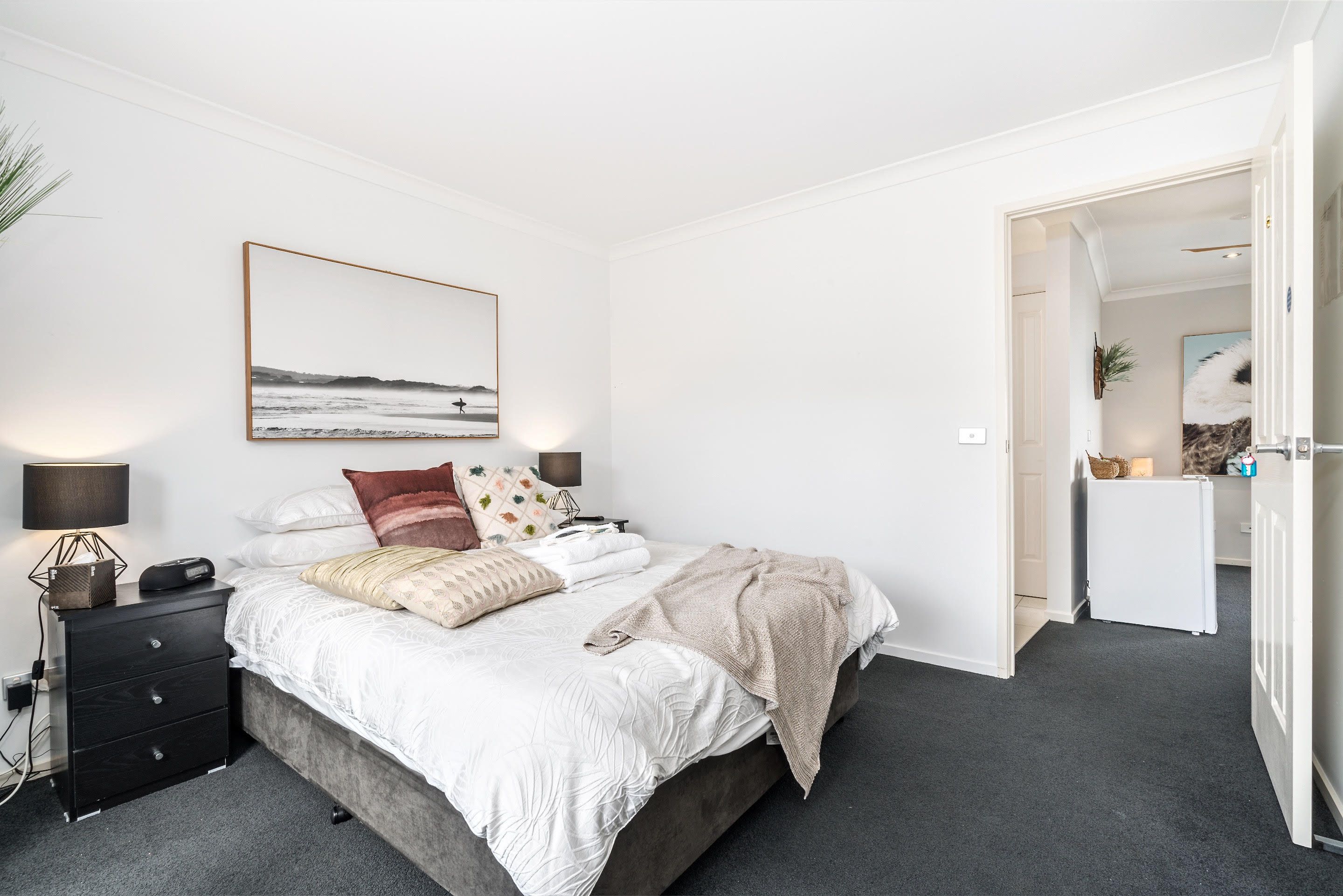 Un dormitorio con cama, mesita de noche, lámpara y un cuadro en la pared.