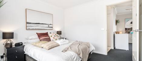 Un dormitorio con cama, mesita de noche, lámpara y un cuadro en la pared.