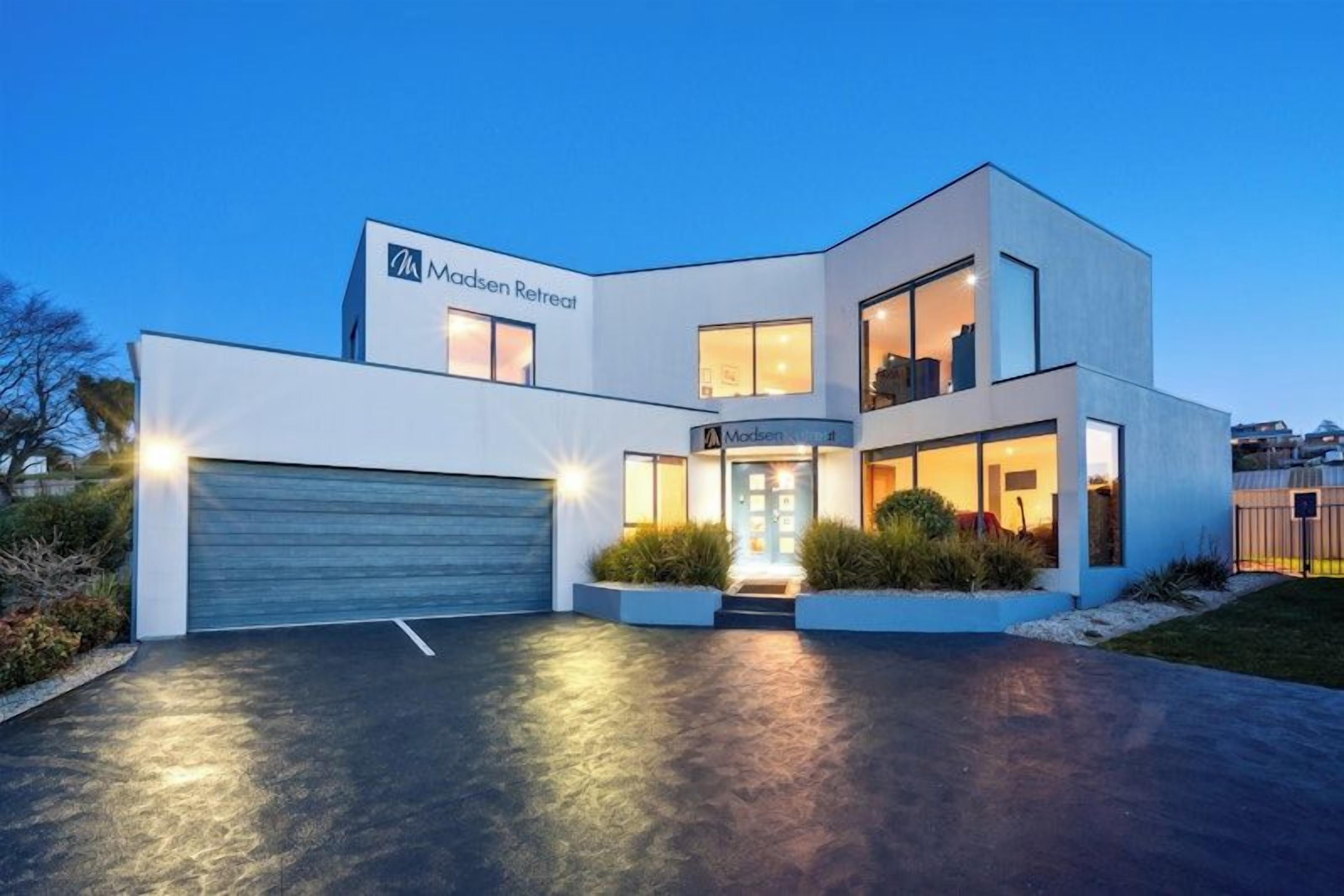 A modern two-story building with a garage, a well-lit entrance, and a landscaped front yard.