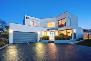 A modern two-story building with a garage, a well-lit entrance, and a landscaped front yard. - Madsen Retreat (Penguin)