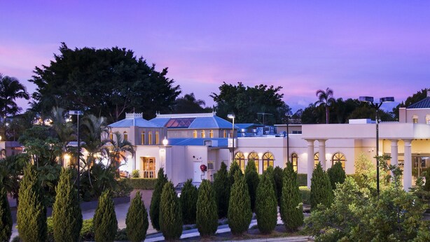 A hotel with a modern architectural style, featuring a central courtyard with neatly trimmed trees and a well-lit entrance. - Shangri La Gardens (Wynnum West)