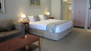 A hotel room with a bed, a sofa, a wooden table, and a painting on the wall. - Shangri La Gardens (Wynnum West)