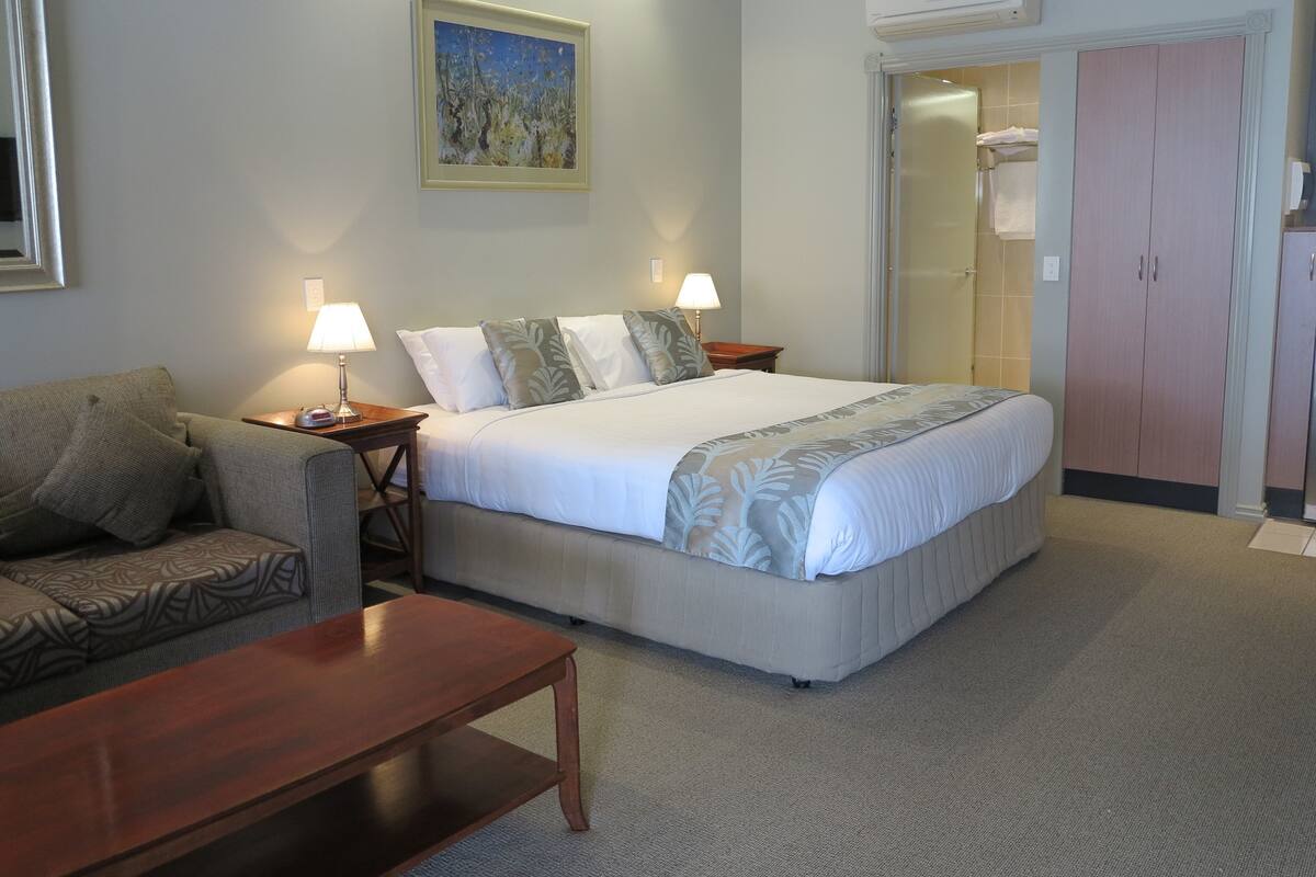 A hotel room with a bed, a sofa, a wooden table, and a painting on the wall.