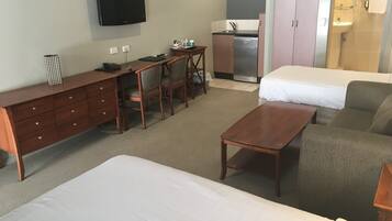 A hotel room with a bed, a desk with a chair, a small kitchenette, and a TV mounted on the wall.