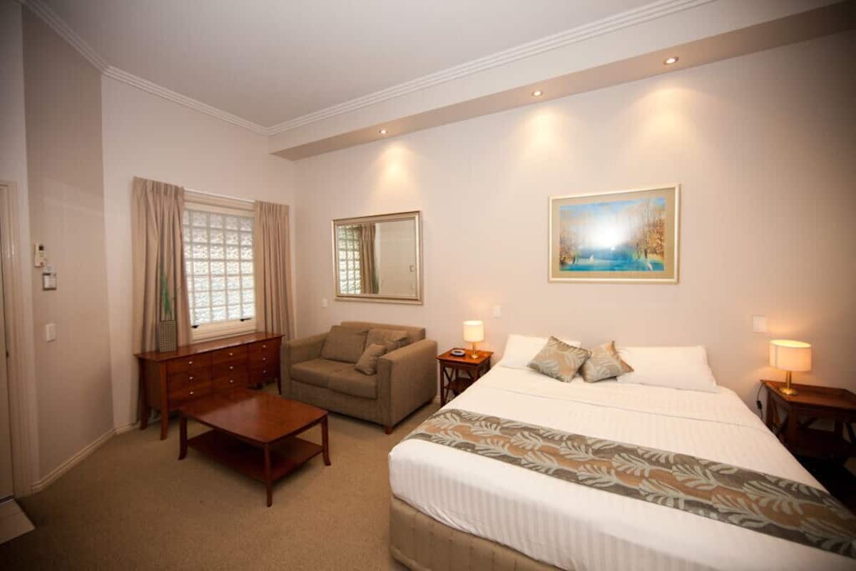 A hotel room with a large bed, a wooden desk, a sofa, a dresser, and a painting on the wall.