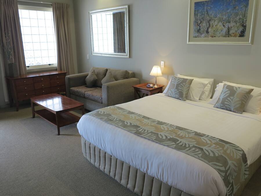 A hotel room with a large bed, a sofa, a wooden desk, and a lamp.