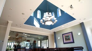 A spacious lobby with a high ceiling, a chandelier, a large sofa, and a framed artwork on the wall. - Shangri La Gardens (Wynnum West)