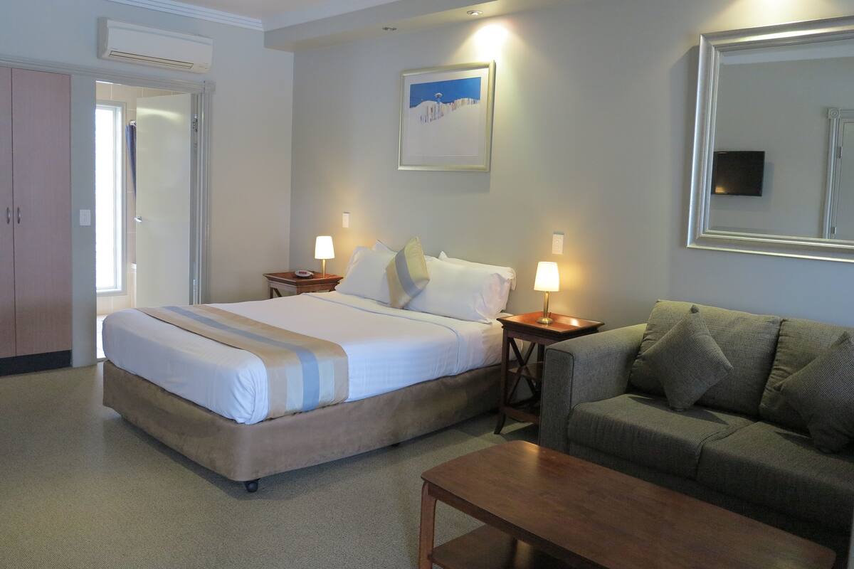 A hotel room with a bed, a sofa, a coffee table, and a painting on the wall.