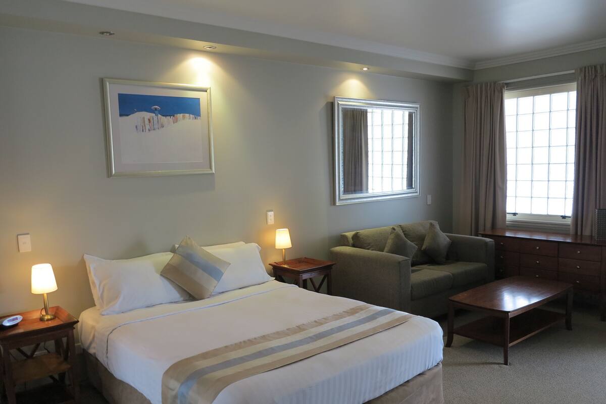 A hotel room with a bed, a sofa, a coffee table, and a window with curtains.