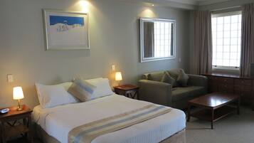 Habitación de hotel con cama, sofá, mesa de centro y ventana con cortinas.