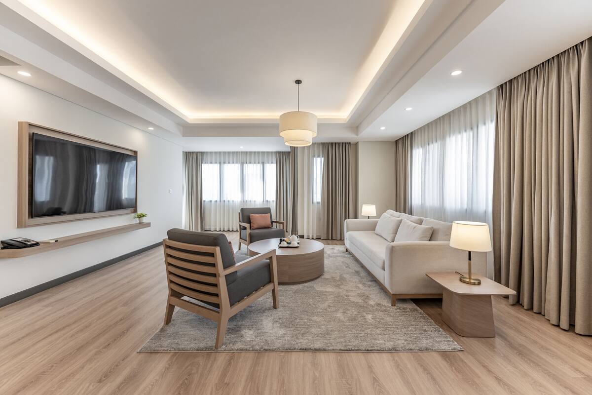 Une chambre d’hôtel moderne équipée d’un grand téléviseur à écran plat, d’un canapé, d’un fauteuil, d’une table basse et d’une lampe.