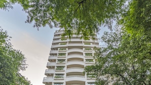 Een hoog hotel met een opvallende entree, meerdere balkons en weelderige beplanting rond de voet.