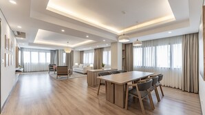Een ruime woonkamer met een houten eettafel, banken en een groot raam met gordijnen.