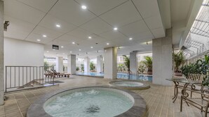 Ruim binnenzwembad met twee whirlpools, een zithoek met stoelen en tafels, en uitzicht op het zwembad door een glazen dak.