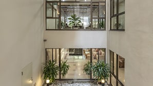 Een moderne binnentuin met een fontein in het midden, meerdere verdiepingen en potplanten.