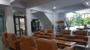 A spacious living area with leather sofas and a coffee table, a piano, and a large window with a view of greenery. - Veethara Boutique Hotel (Udon Thani)