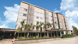A modern hotel with a multi-story structure, featuring a central vertical design element, a covered entrance, and a landscaped front with palm trees. - Veethara Boutique Hotel (Udon Thani)