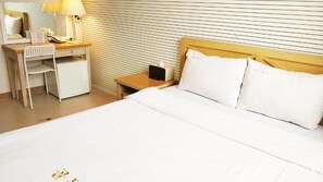 Een hotelkamer met een bed, een bureau met stoel, een nachtkastje en een lamp.