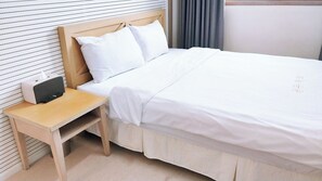 Una cama bien hecha con sábanas blancas, una mesita de noche de madera con un control remoto y una mesilla.