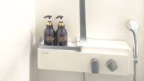 A shower with a handheld showerhead, a control panel, and two bottles of shampoo and body wash.