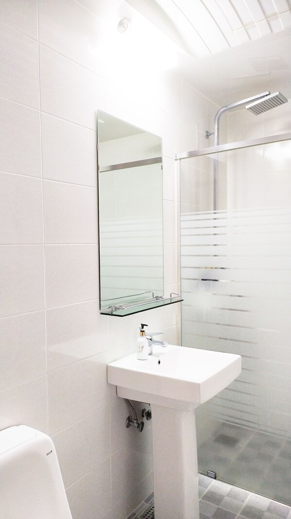 Un baño moderno con lavamanos blanco, cabina de ducha de vidrio y espejo sobre el lavamanos.