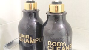 Two black bottles with gold caps labeled "Hair Shampoo" and "Body Cleanser" on a white shelf.