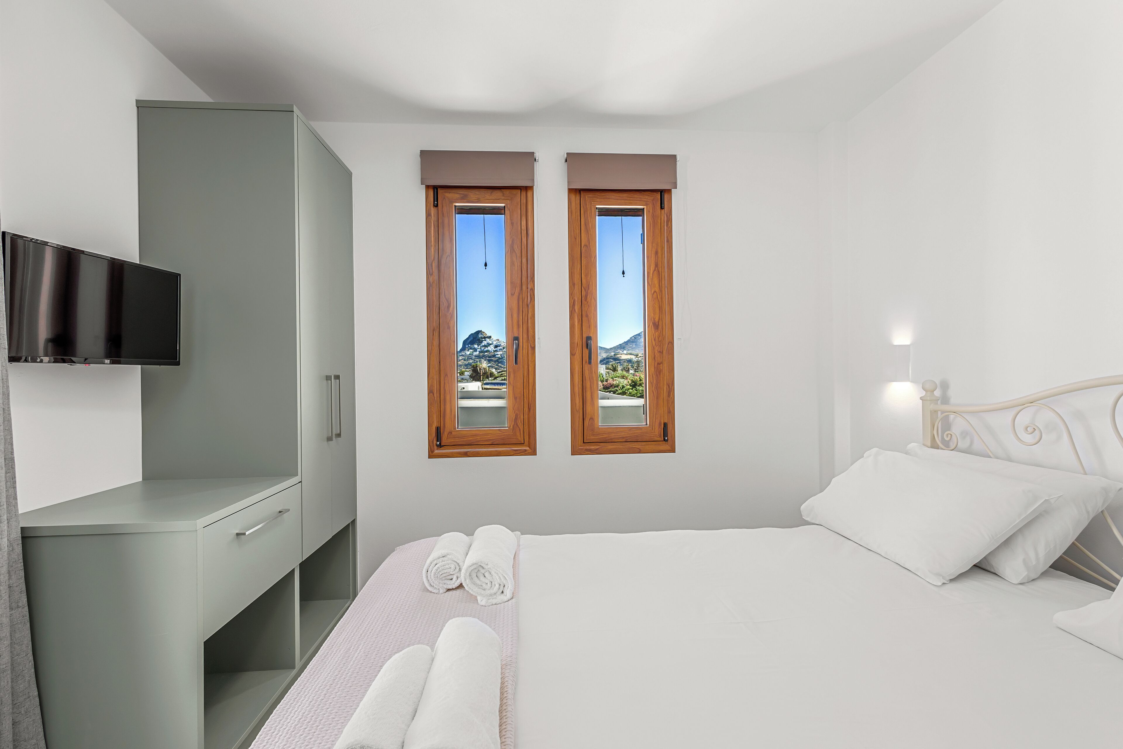 Une chambre à coucher avec un lit, deux fenêtres, une télévision et une armoire.