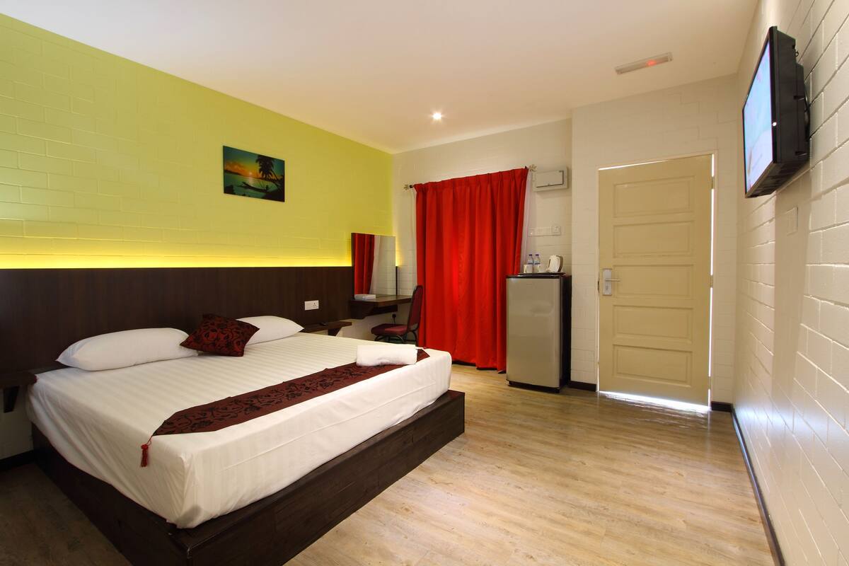 Una habitación de hotel con cama, escritorio, silla, televisor y puerta.