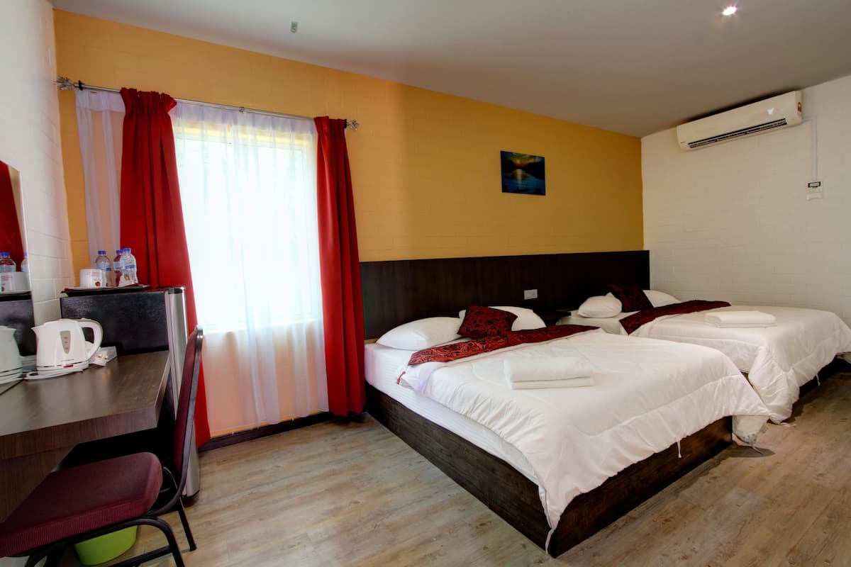 Habitación de hotel con dos camas, un escritorio con silla, cafetera y ventana con cortinas rojas.