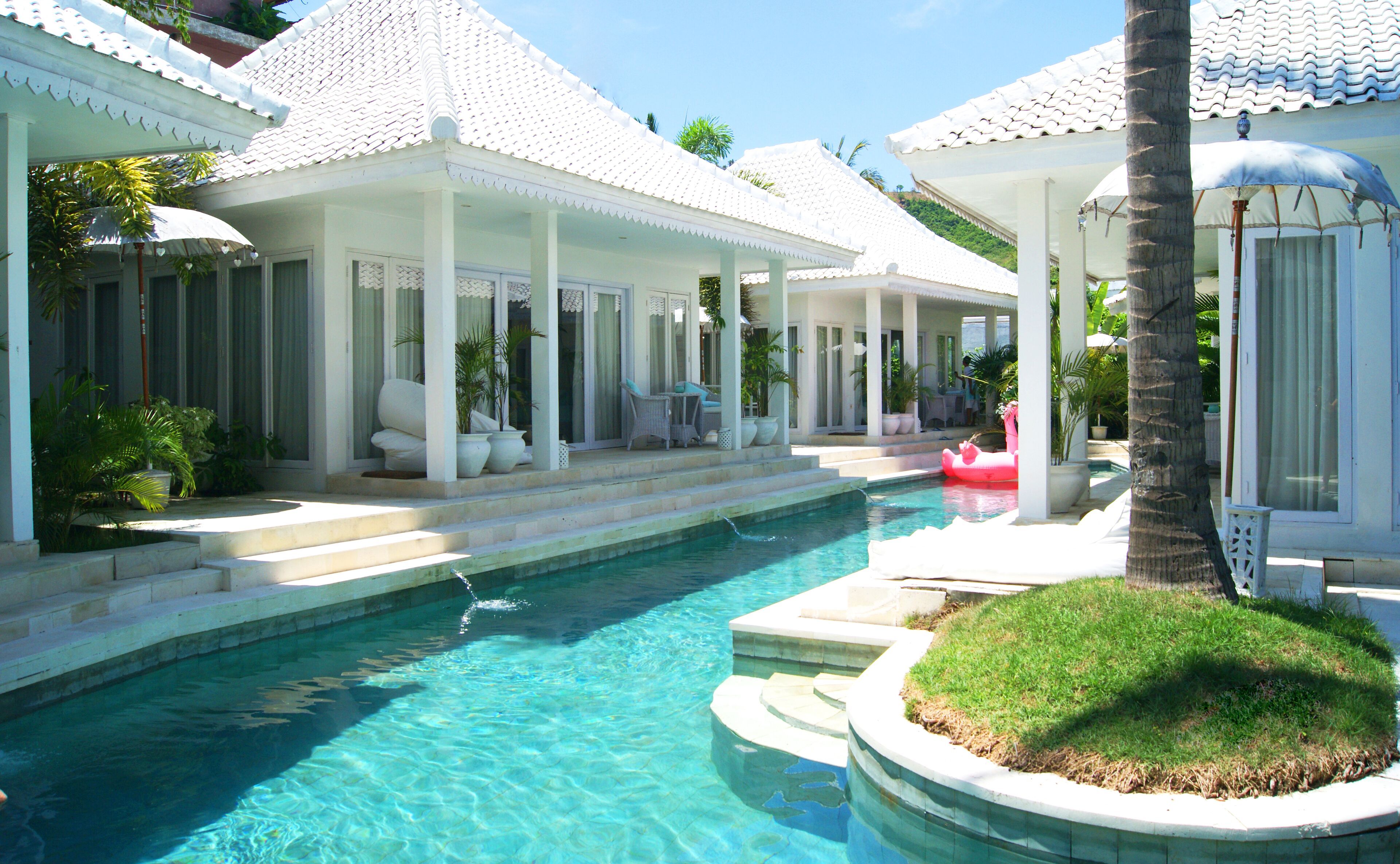 A pool area with a clear blue pool, white tiled roofs, and outdoor seating areas.