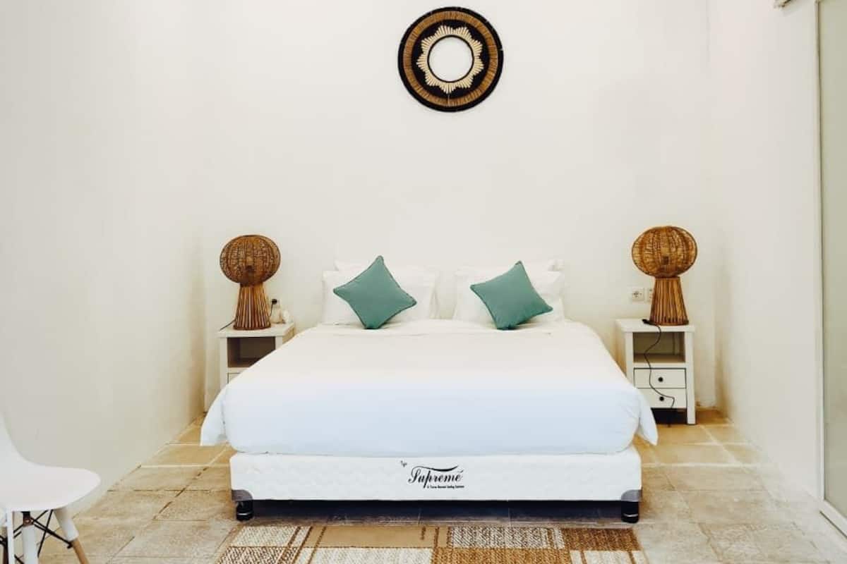 Un dormitorio con una cama, dos mesitas de noche, aire acondicionado instalado en la pared y un espejo decorativo.