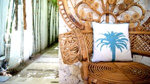 A wicker chair with a palm tree pillow, set against a stone wall with a bamboo fence in the background. - Harmony Villas Lombok (Kuta)