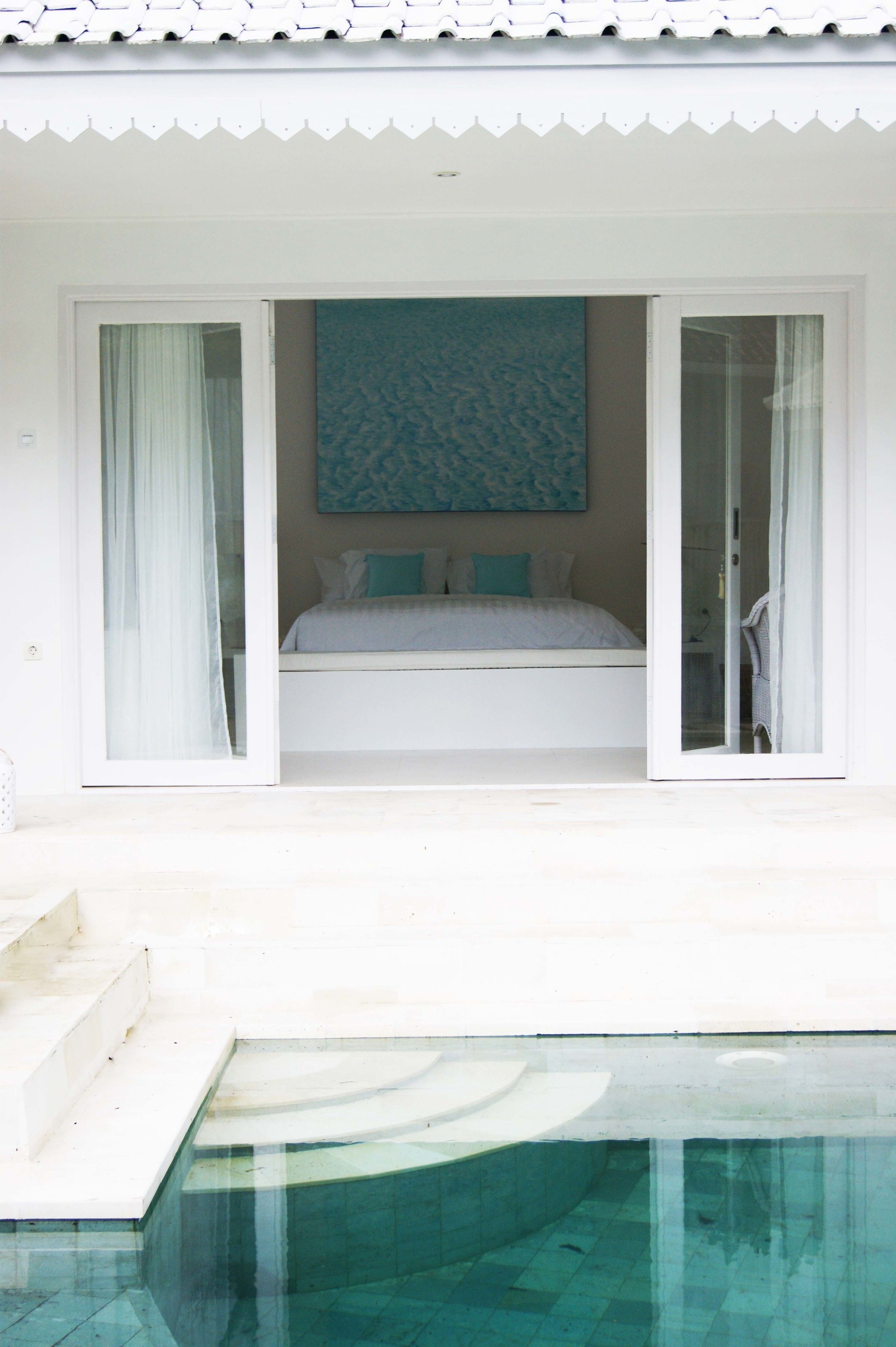 A bedroom with a bed, a large window, and a view of a swimming pool.